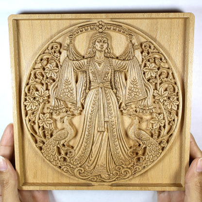 Anahita wood relief held in hands for size reference, showing the square frame, goddess carving, peacocks, and natural beech wood.