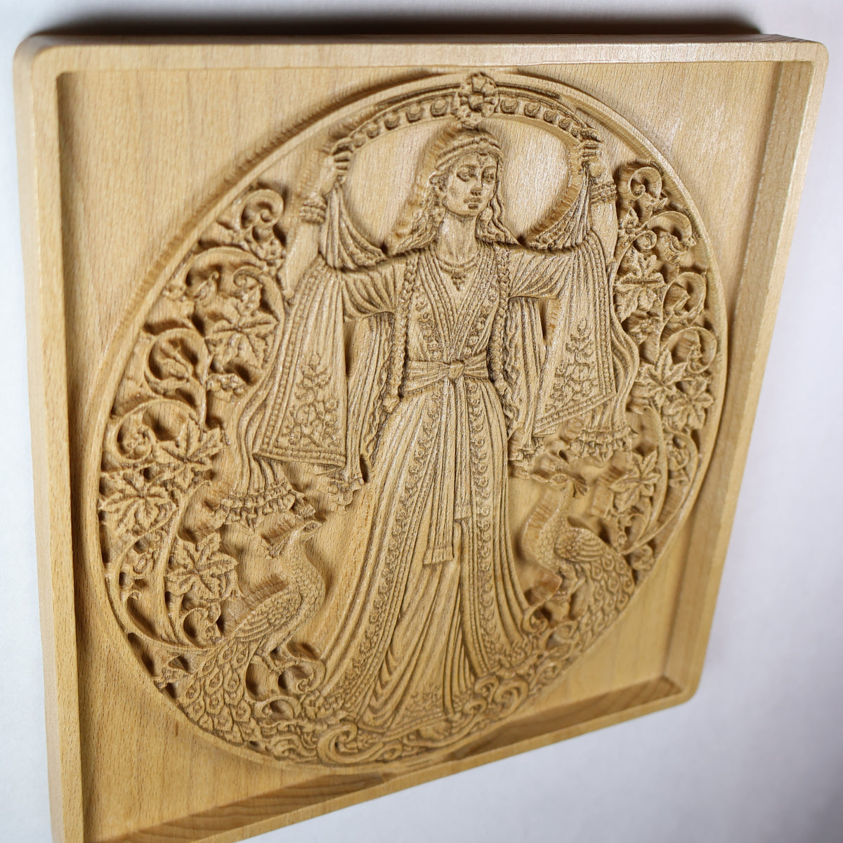 Side view of the Anahita wood relief showing the raised goddess figure, carved birds, botanical details, panel depth, and natural wood finish.