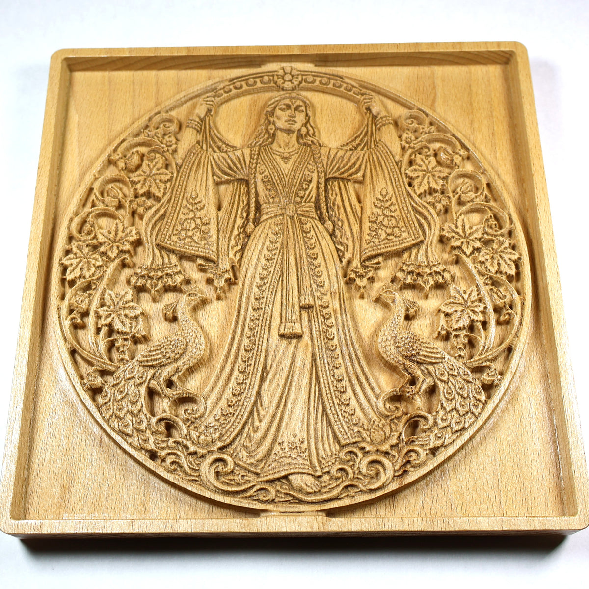Low angled view of the Anahita relief showing the flowing robe, peacocks, floral carving, round frame, and raised wood detail.