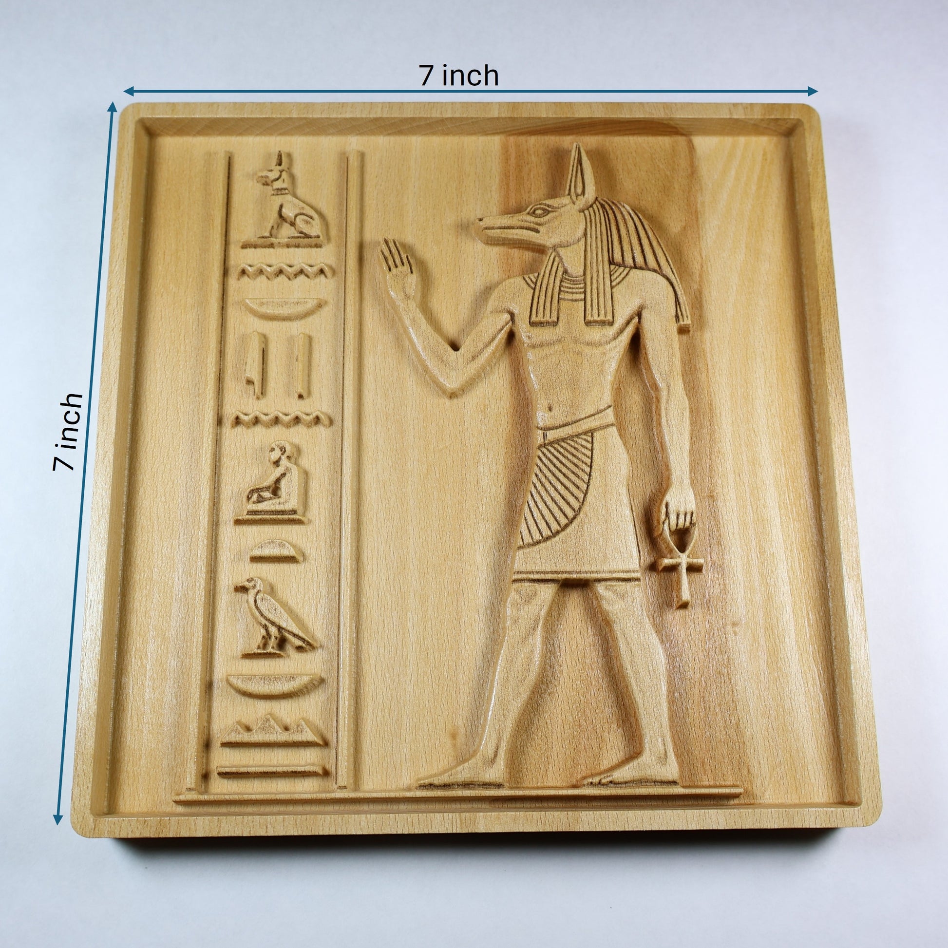 Anubis wood relief with 7 inch width and height markers, showing the carved Egyptian figure, ankh, hieroglyphic details, and natural wood finish.