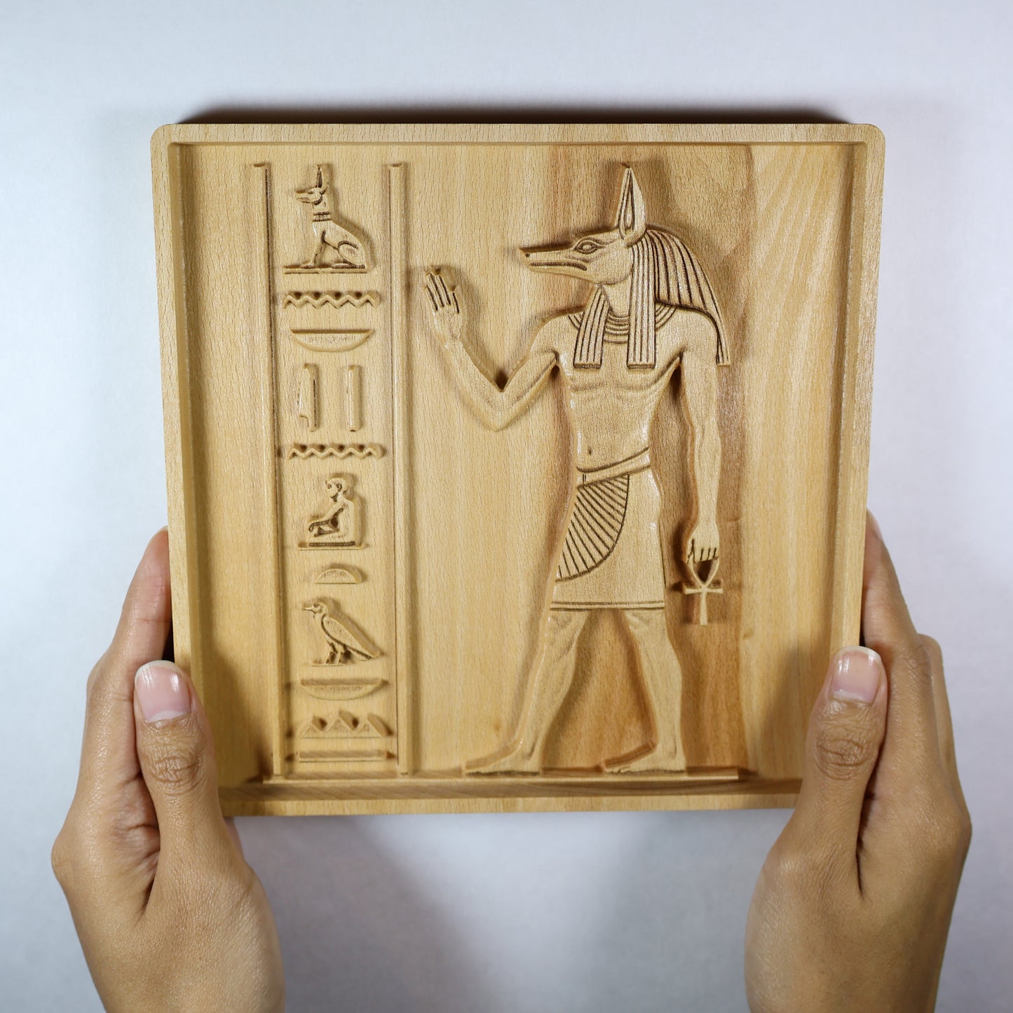 Anubis wood relief held in hands, showing the size, carved Egyptian figure, hieroglyphic details, and natural wood finish.