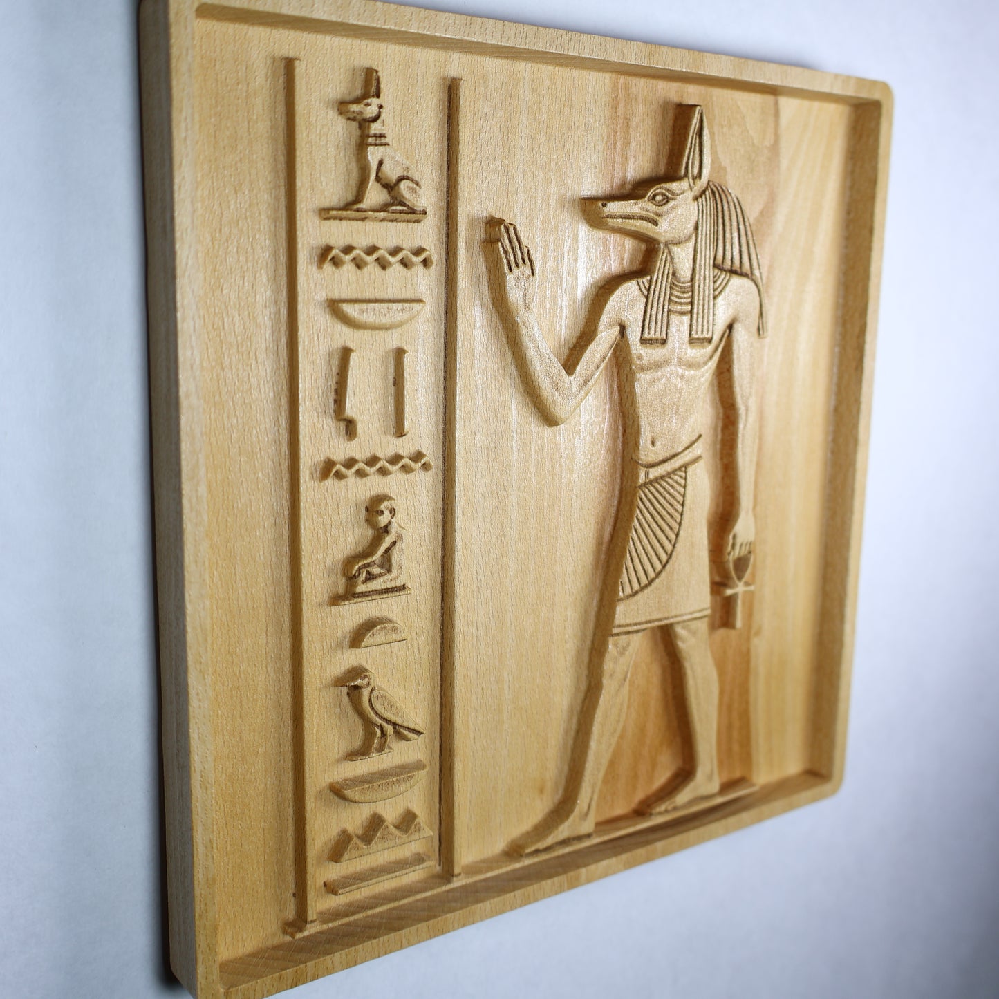 Side view of an Anubis wood relief showing the panel thickness, raised carving depth, hieroglyphic details, and natural wood edge.