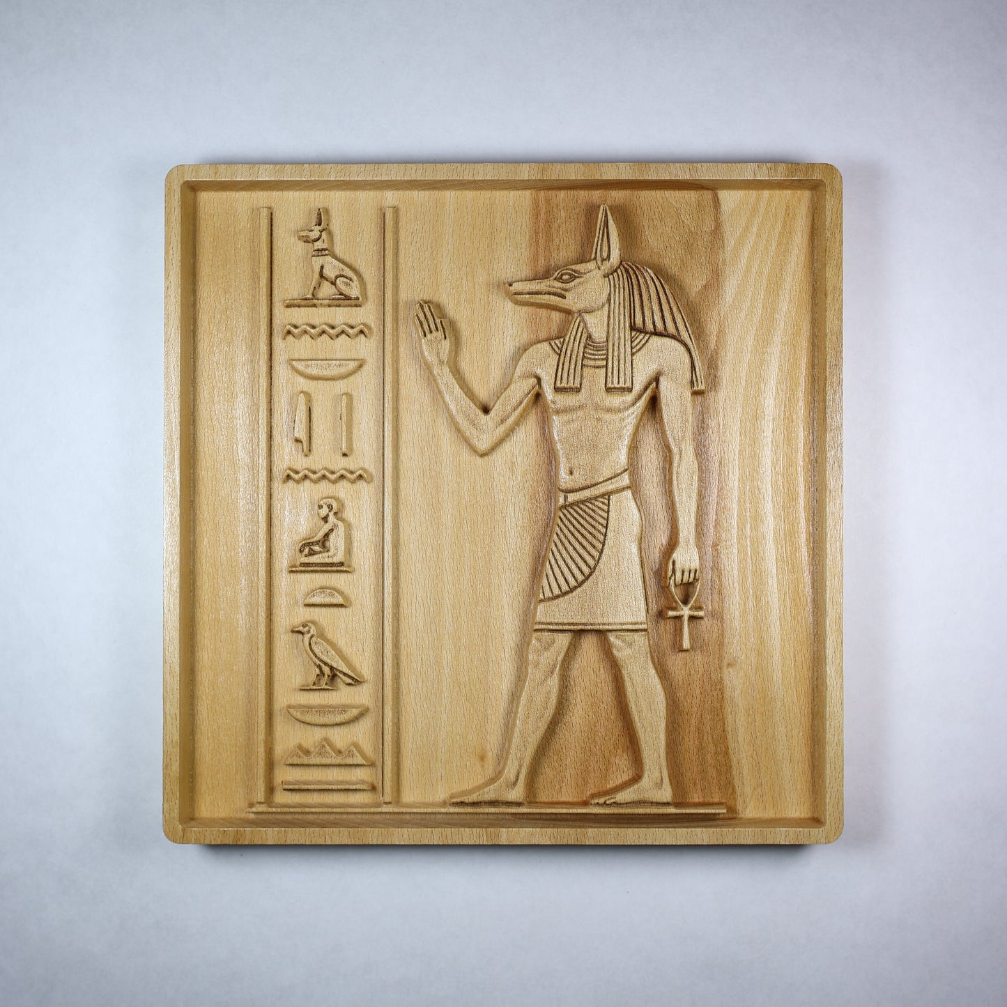 Front view of an Anubis wood relief showing the jackal-headed figure, raised hand, ankh, hieroglyphic details, and natural wood finish.