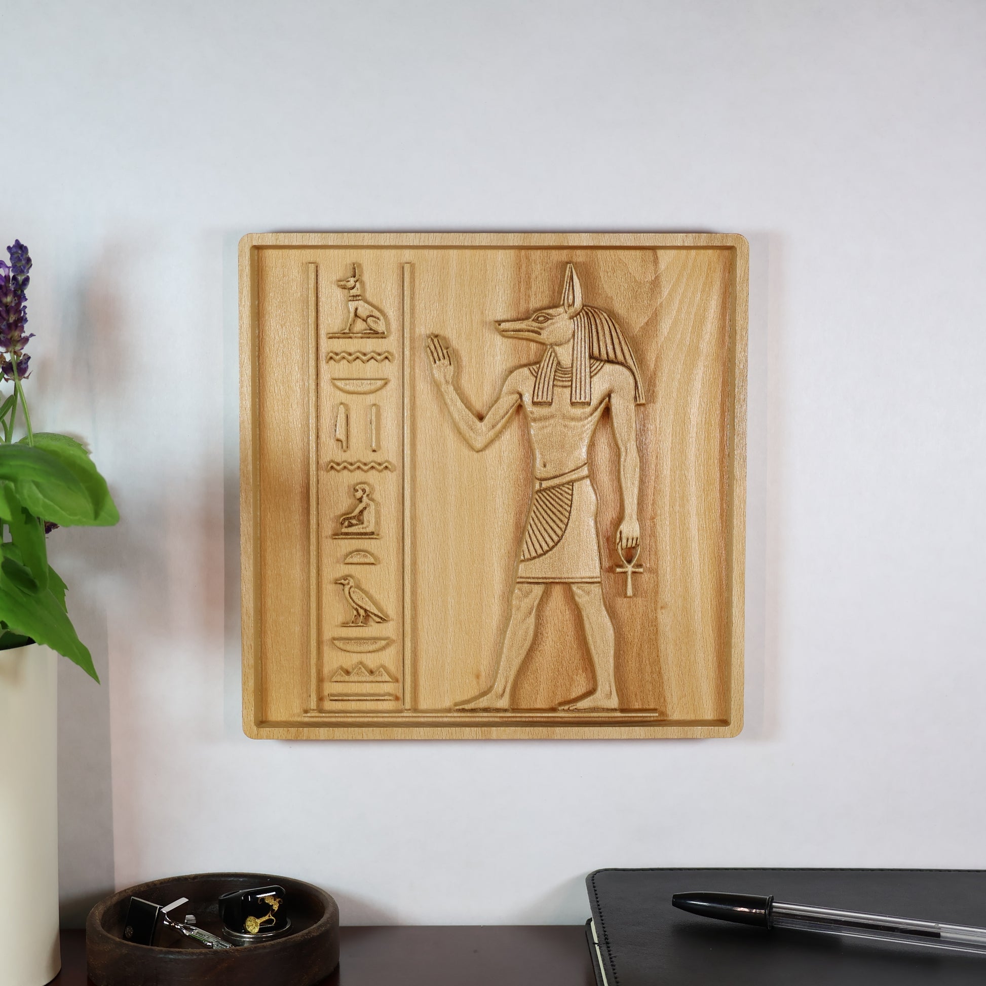 Anubis wood relief displayed on a wall in a modern room, showing the carved Egyptian figure and natural wood finish.