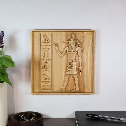 Anubis wood relief displayed on a wall in a modern room, showing the carved Egyptian figure and natural wood finish.
