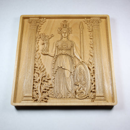 Low angled view of an Athena wood carving showing the goddess, shield, spear, layered robe details, raised relief, and natural wood grain.
