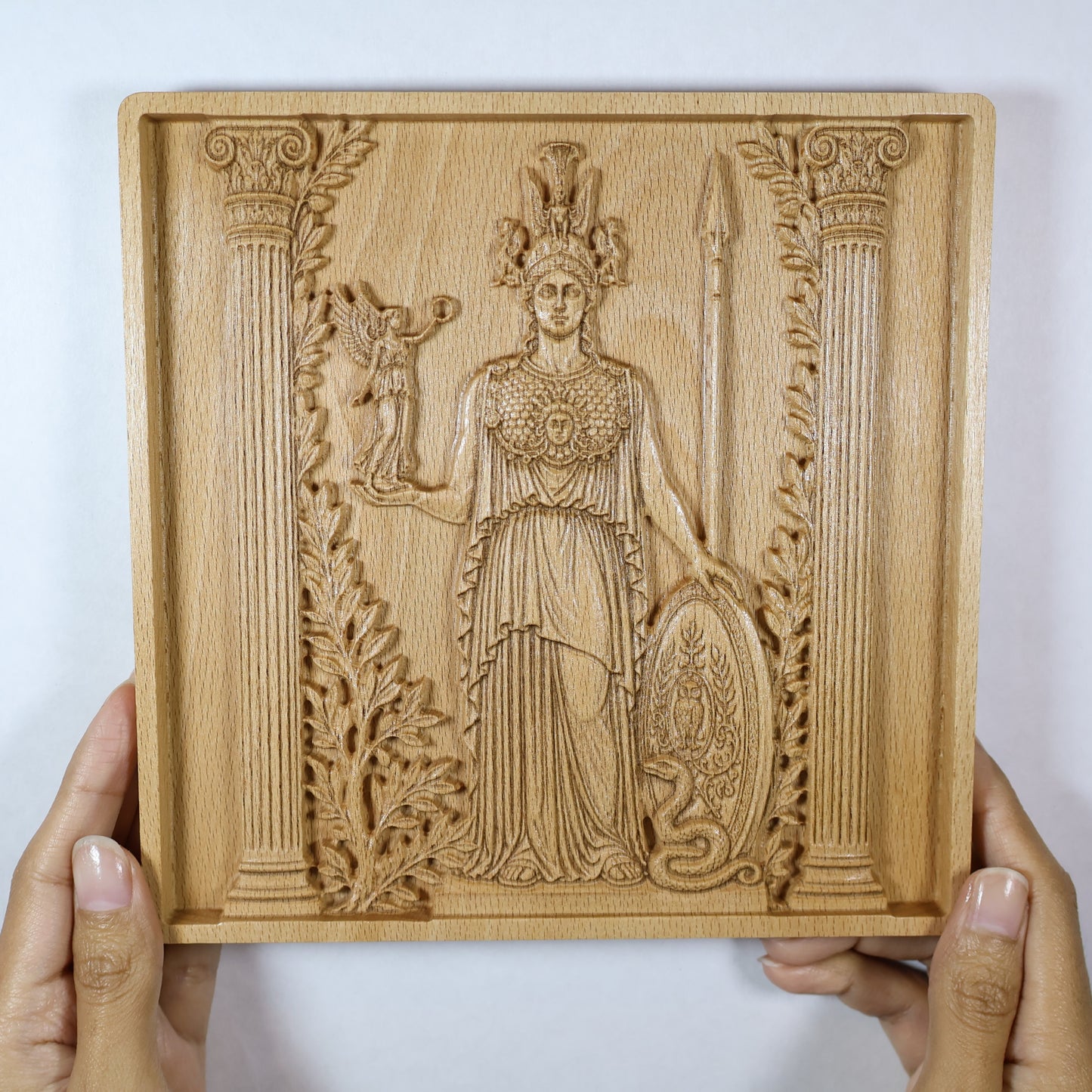 Athena wood relief held in hands for size reference, showing the framed Greek goddess carving and natural beech wood finish.