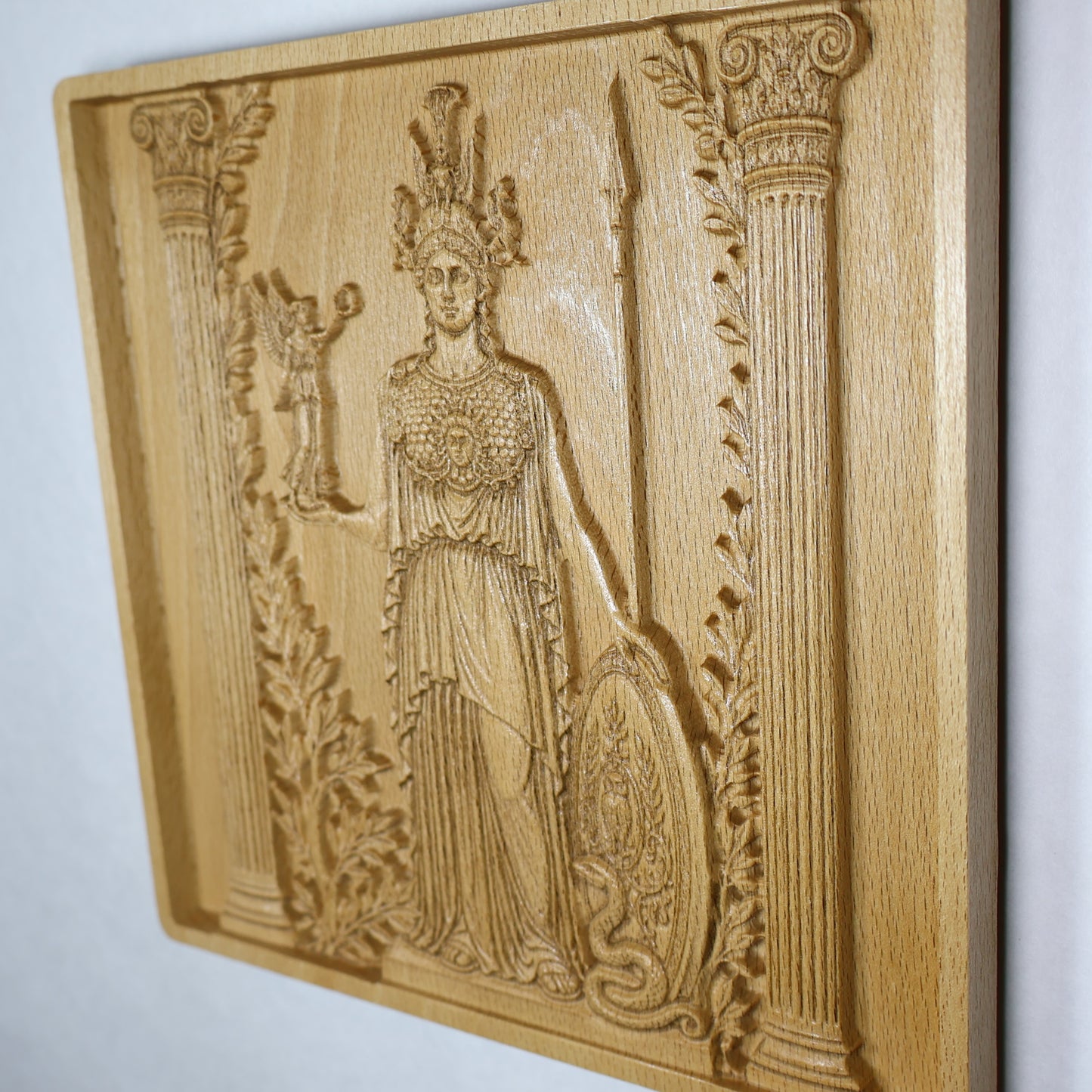Three-quarter view of the Athena carving showing classical Greek details, olive foliage, raised surfaces, and natural beech wood texture.