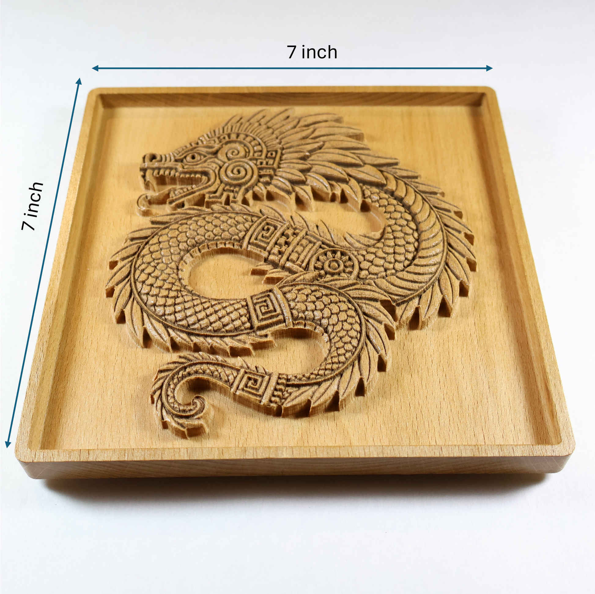 Size reference for Quetzalcoatl beech wood wall art showing 7 inch by 7 inch square carved plaque with raised feathered serpent relief, recessed border frame, visible plaque thickness, and warm natural wood finish