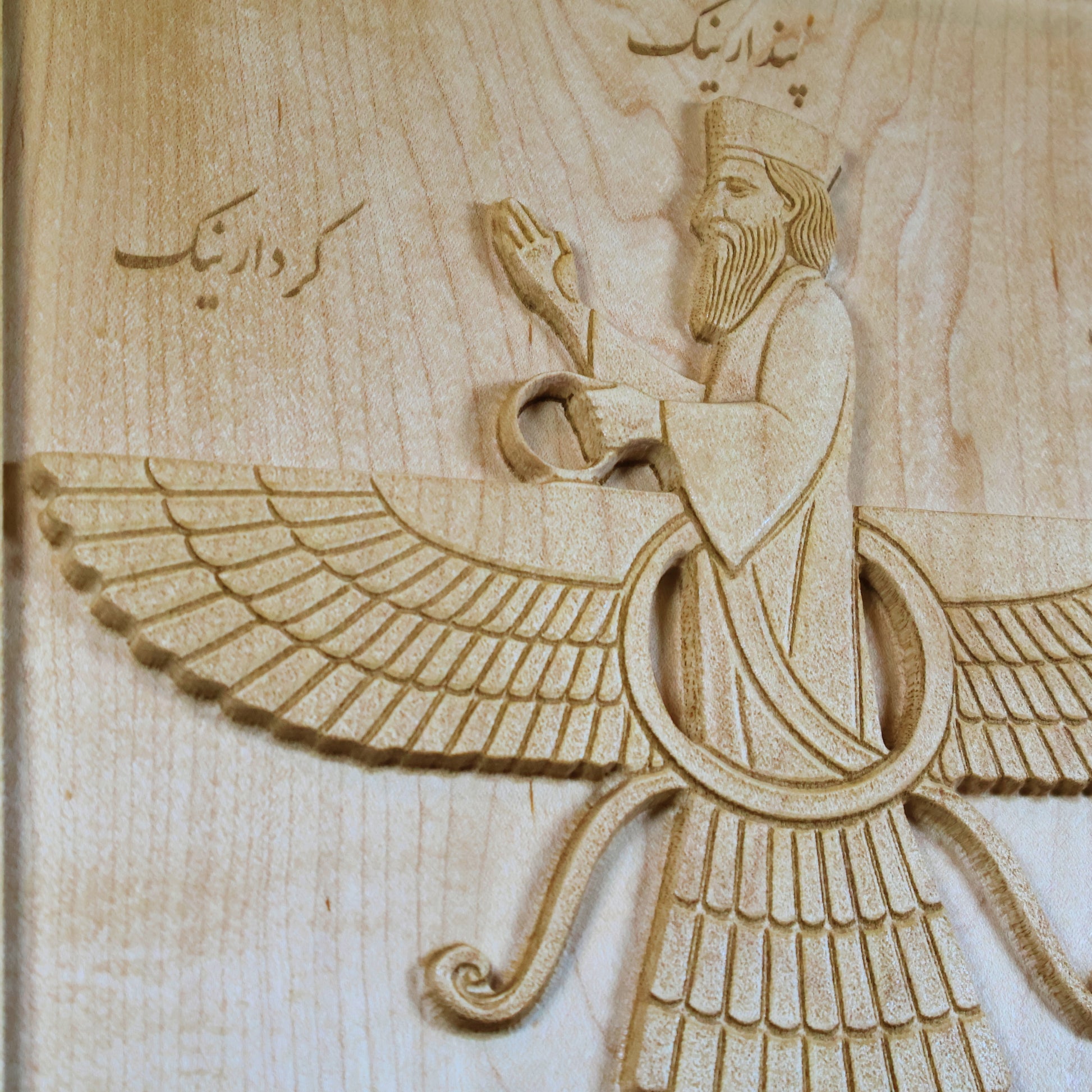 Close-up of the Faravahar carving showing the central figure, layered wings, ribbons, Farsi inscription, and fine maple wood grain.