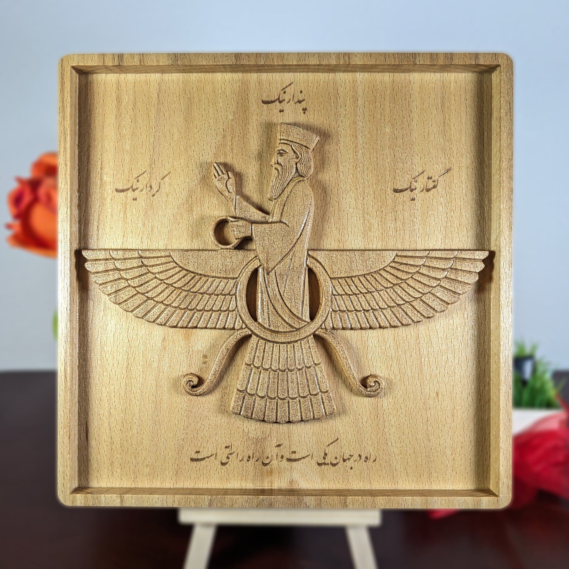 7x7 Faravahar wood wall art displayed on a small easel with soft home decor background, showing Persian carved wood relief, Farsi calligraphy, extended wings, central figure, and framed solid beech panel for office desk, shelf, or tabletop display.