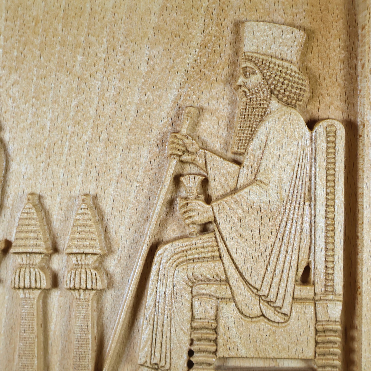 Macro detail of the Persepolis Royal Audience wood relief showing King Darius seated on the throne with staff and cup, ceremonial stands, carved robe lines, and natural beech wood finish.