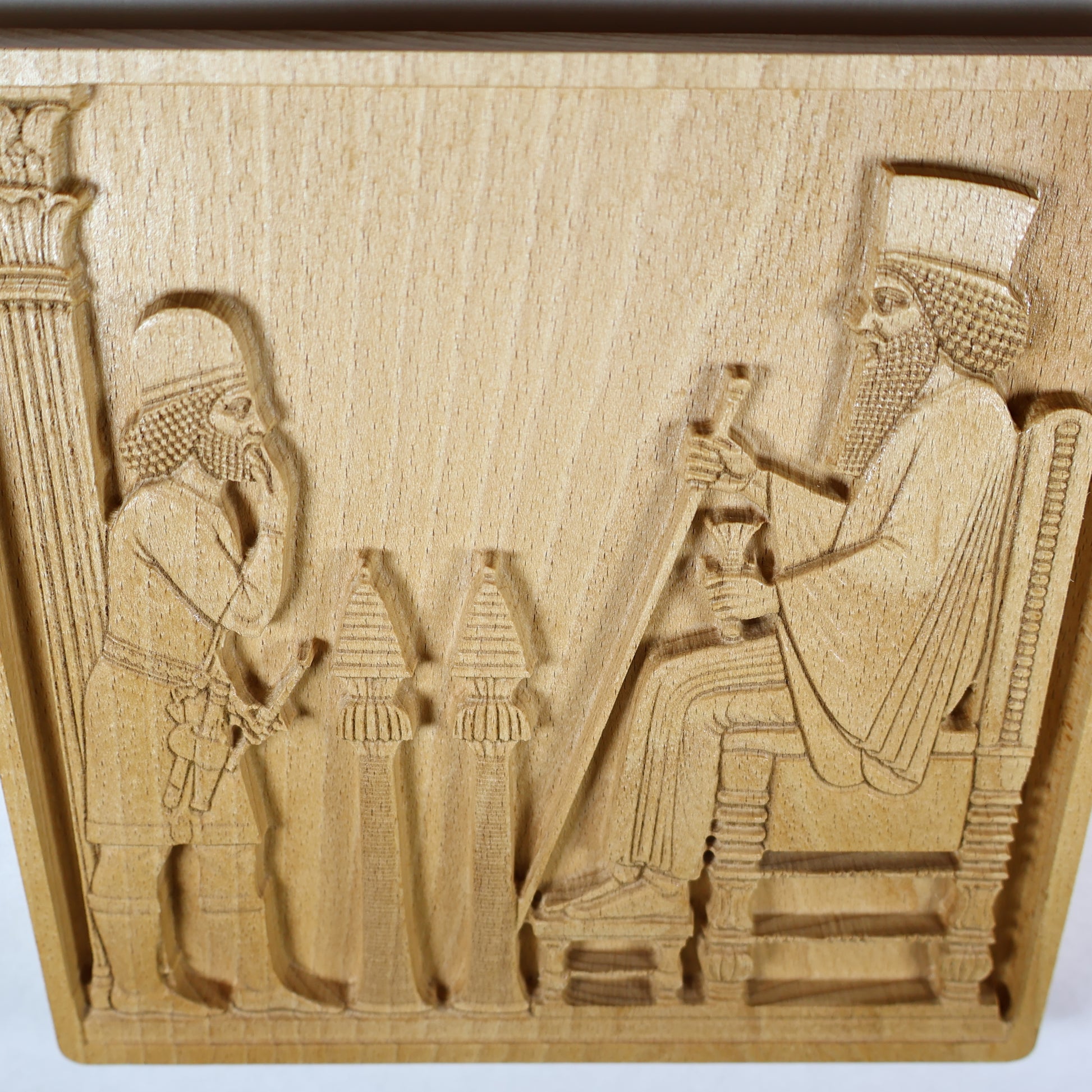 Overhead angled view of the Persepolis Royal Audience wood relief showing the seated king, approaching figure, ceremonial stands, throne, column edge, and natural beech wood finish.