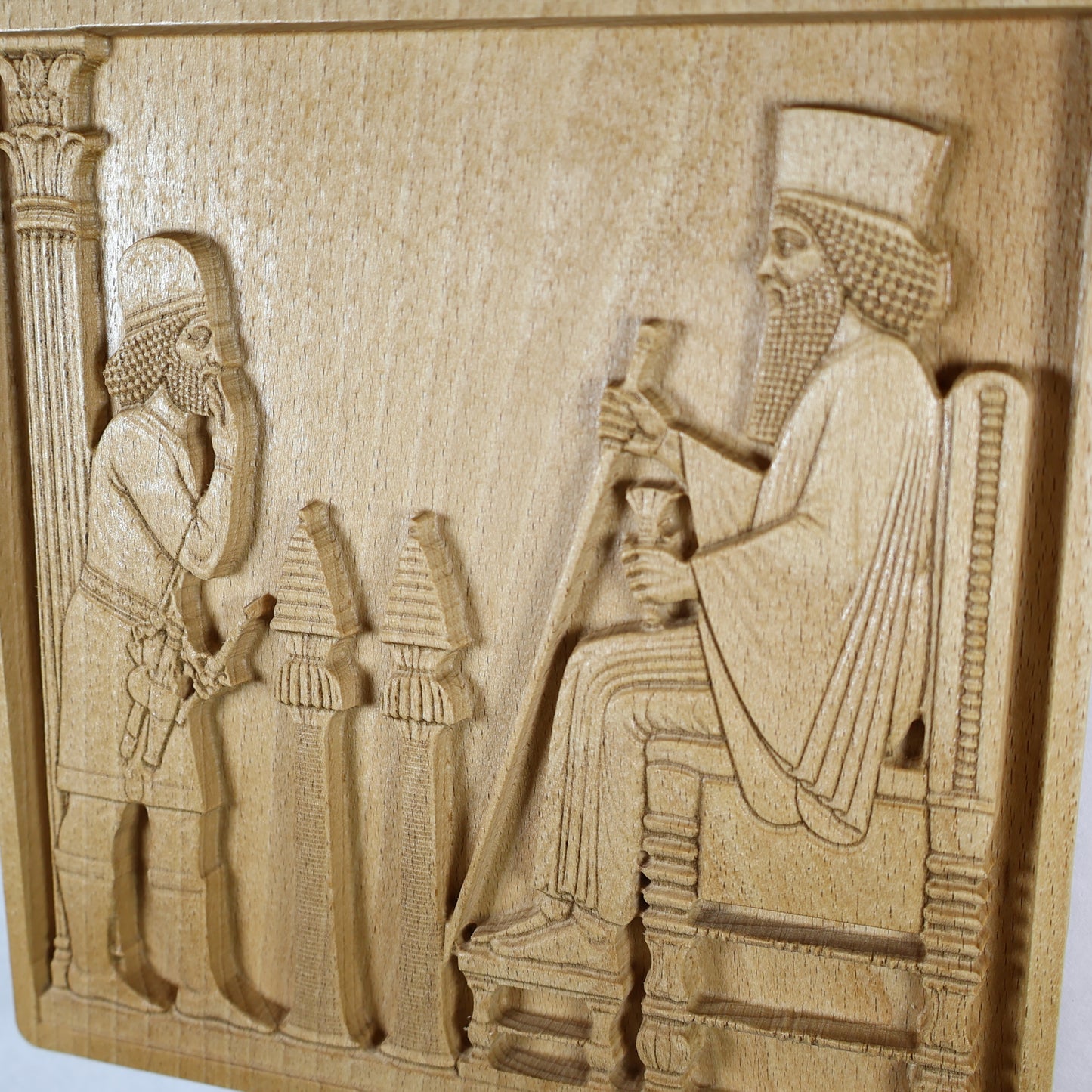 Close angled view of the Persepolis Royal Audience wood relief showing the seated king, respectful attendant, palace column, ceremonial objects, throne rail, and natural beech wood finish.