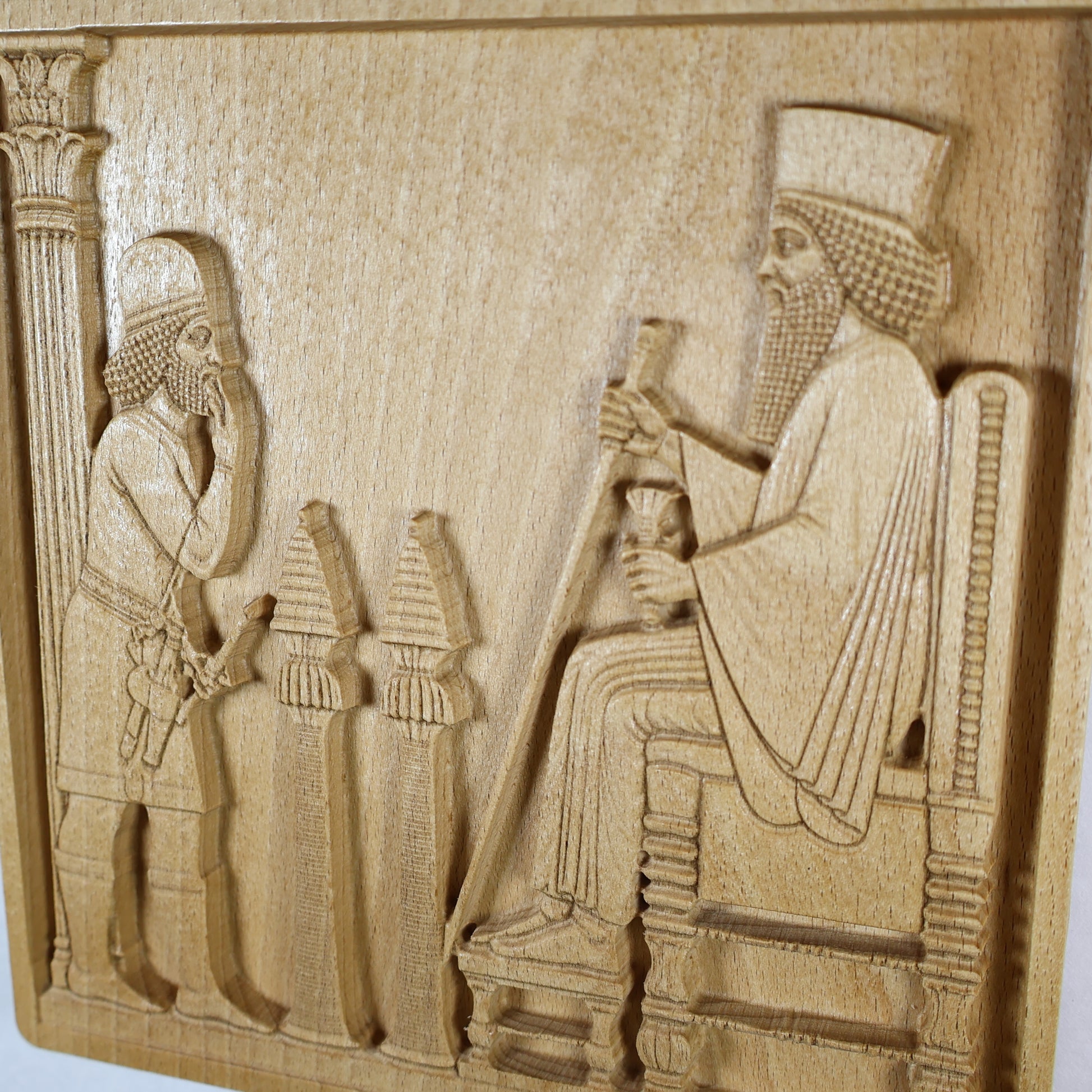 Close angled view of the Persepolis Royal Audience wood relief showing the seated king, respectful attendant, palace column, ceremonial objects, throne rail, and natural beech wood finish.