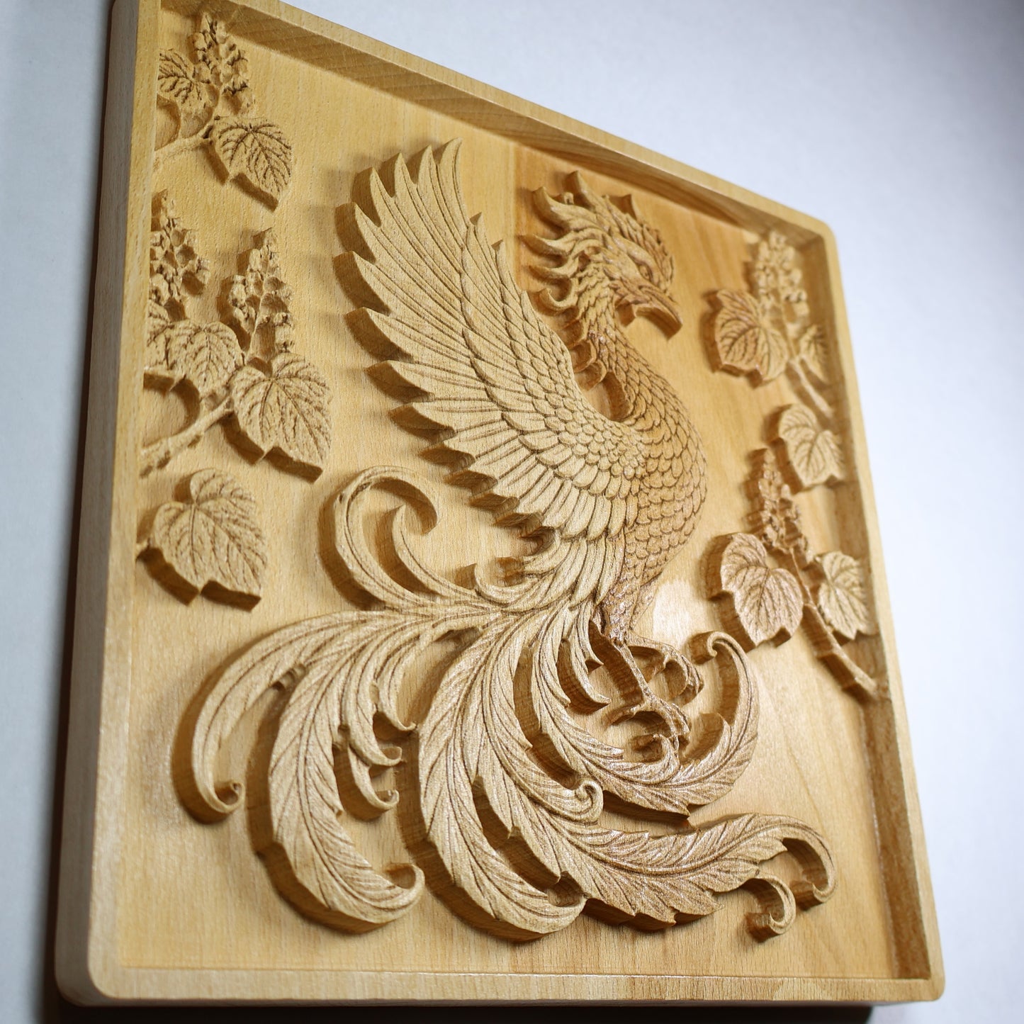 Angled close view of a Japanese Phoenix wood relief showing the raised bird carving, layered feathers, paulownia details, and natural wood finish.