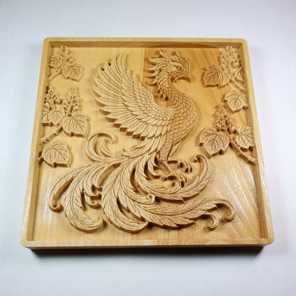 Low angled view of a Hoo Phoenix wood relief showing the raised wing, curled tail feathers, paulownia branches, and natural wood grain.