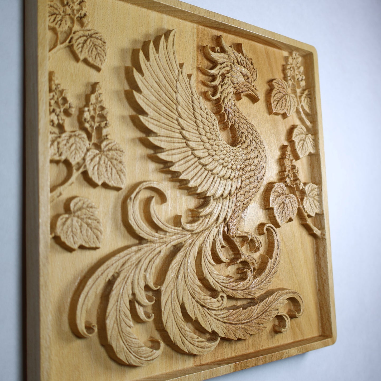Left side display view of a Japanese Phoenix wood relief showing the raised wing, flowing tail, paulownia branches, and natural wood finish.