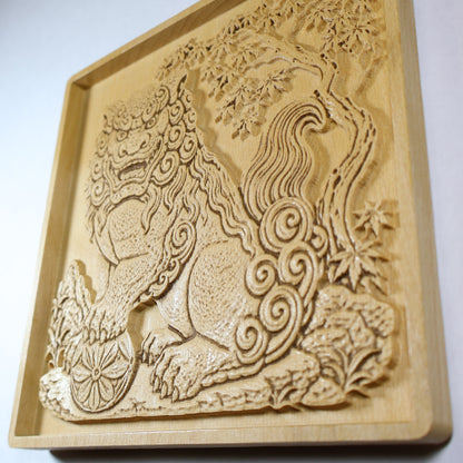 Side angle view of a Japanese Komainu guardian lion dog wood relief showing the raised carving depth, curled tail, floral ball, maple tree, and natural wood finish.