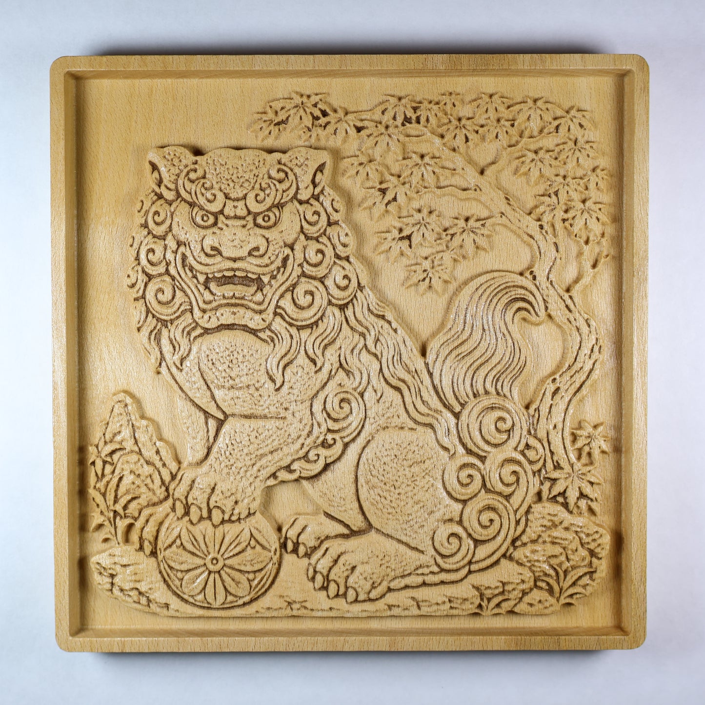 Front view of a Japanese Komainu guardian lion dog wood relief with a carved floral ball, curled mane, maple tree background, square frame, and natural wood finish.
