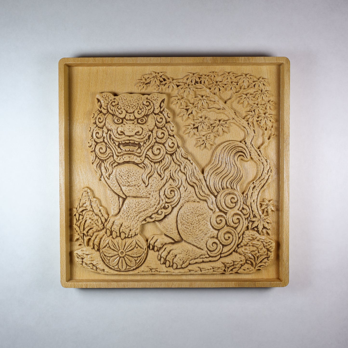 Front view of a Japanese Komainu guardian lion dog wood relief with a carved floral ball, curled mane, tree details, square frame, and natural wood finish.