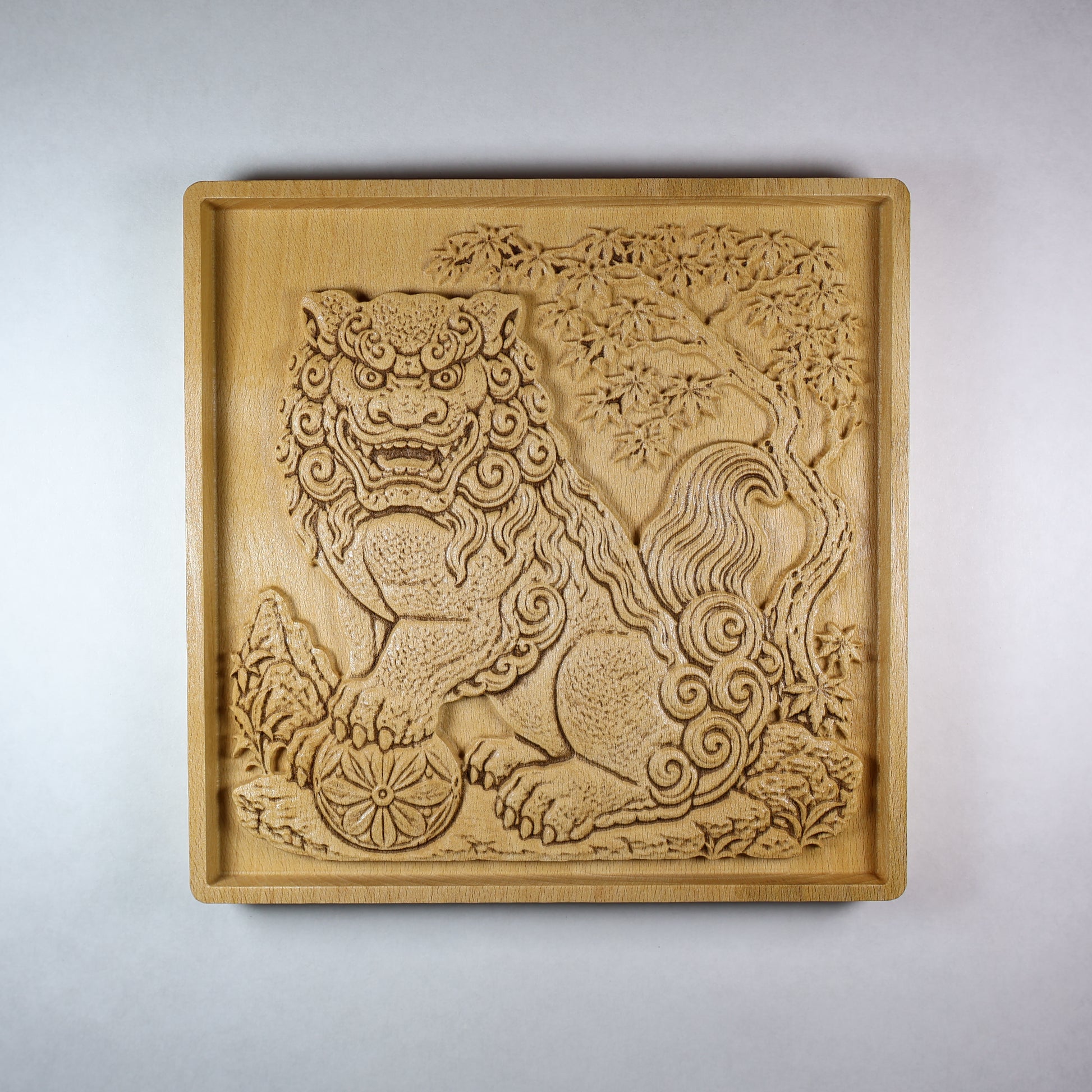 Front view of a Japanese Komainu guardian lion dog wood relief with a carved floral ball, curled mane, tree details, square frame, and natural wood finish.