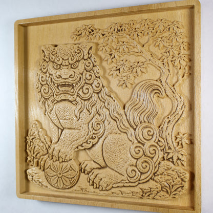 Angled side view of a Japanese Komainu guardian lion dog wood relief showing the carved guardian, floral ball, curled mane and tail, maple tree branches, and natural wood finish.