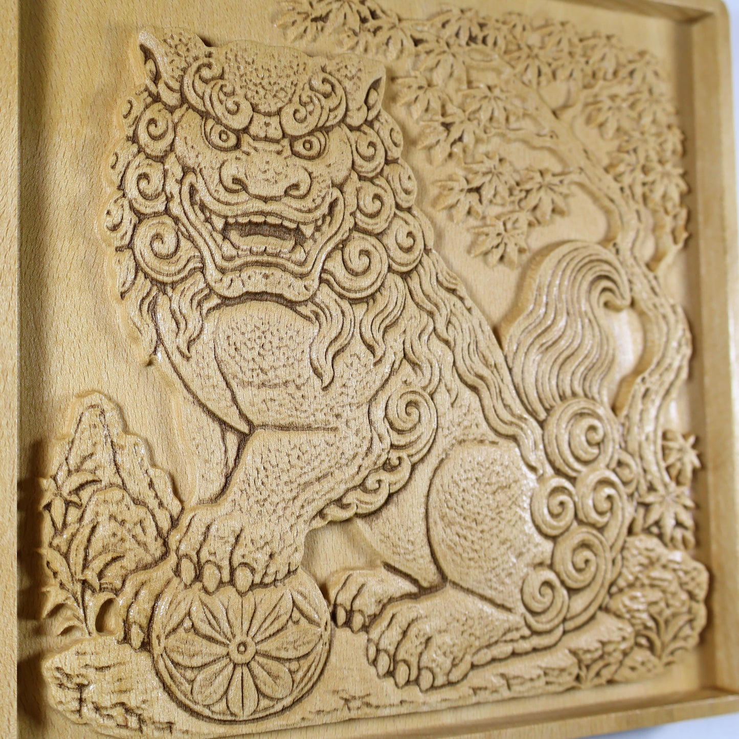 Close detail of a Japanese Komainu wood carving showing the guardian face, spiral mane, textured paws, flower ball, garden plants, and natural wood finish.