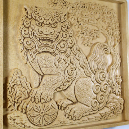 Close detail of a Japanese Komainu wood carving showing the guardian face, spiral mane, textured paws, flower ball, garden plants, and natural wood finish.