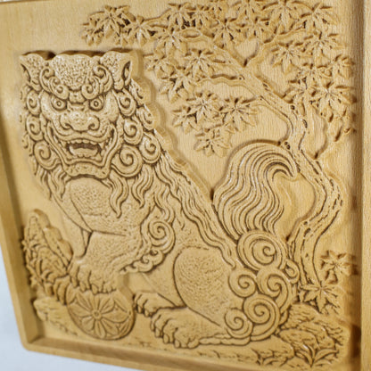 Close side detail of a Japanese Komainu wood relief showing the guardian lion, carved maple tree, flowing tail scrolls, flower ball, and raised natural wood texture.