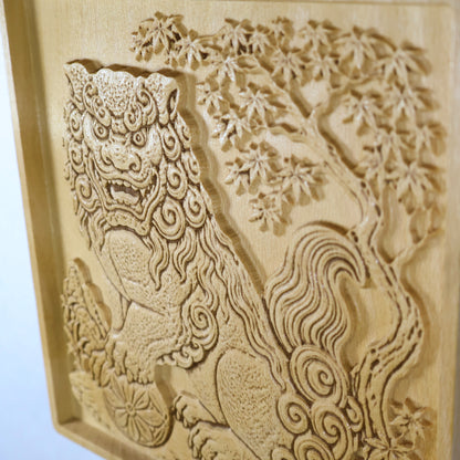 Oblique close-up of a Japanese Komainu wood relief showing the guardian lion, maple tree leaves, curled tail, carved depth, and polished natural wood finish.