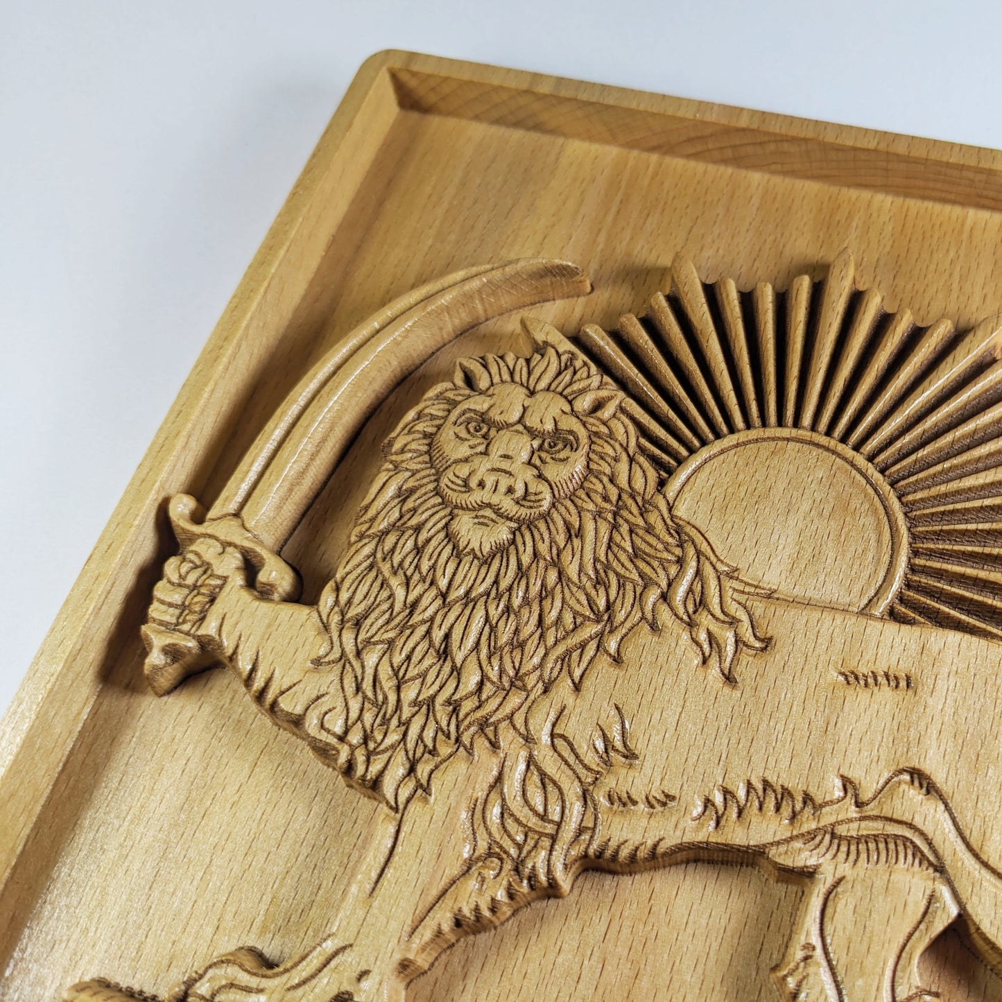 Close-up of Lion and Sun wood wall art carved in solid beech, showing the lion face, flowing mane, curved saber, front paw, radiant sunburst, fine engraved lines, raised relief layers, and warm natural wood surface.