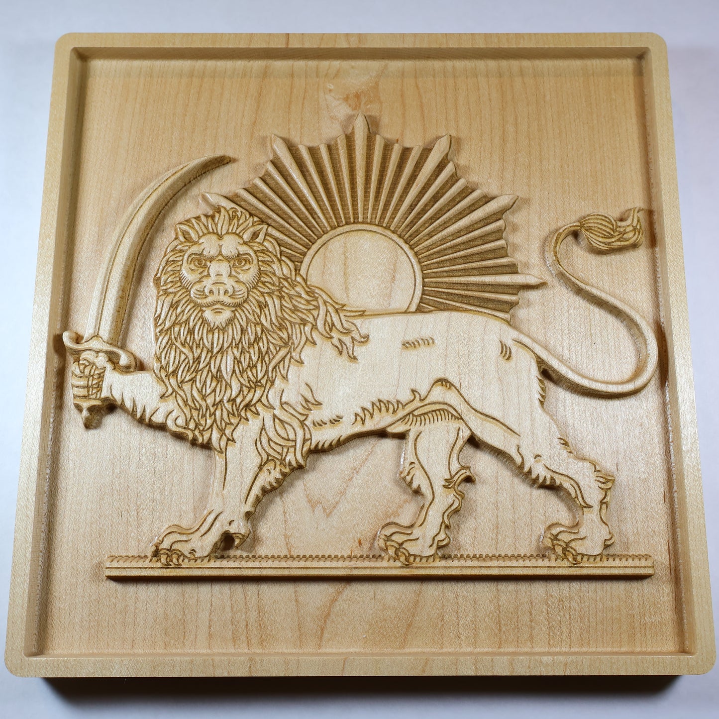 Low angled view of the Lion and Sun relief showing raised carving depth, lion mane, sun rays, sword, and natural maple wood grain.