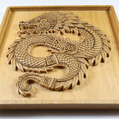 Angled close-up of Quetzalcoatl beech wood relief showing dramatic carved relief depth, feathered serpent head with spiral ornament, layered feather plumes, fish-scale body texture, and geometric Aztec patterning