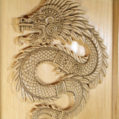 Quetzalcoatl feathered serpent wood relief mounted on wall, side lighting revealing deep carved grooves, coiled serpent body with overlapping scales, geometric Aztec bands, and layered feather detail on solid beech