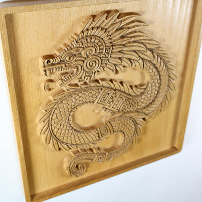 Top-down angled view of Quetzalcoatl beech wood wall plaque showing full serpent body sweep, feathered crest, coiled tail with spiral finial, geometric Aztec neck bands, and deep shadow relief on natural wood