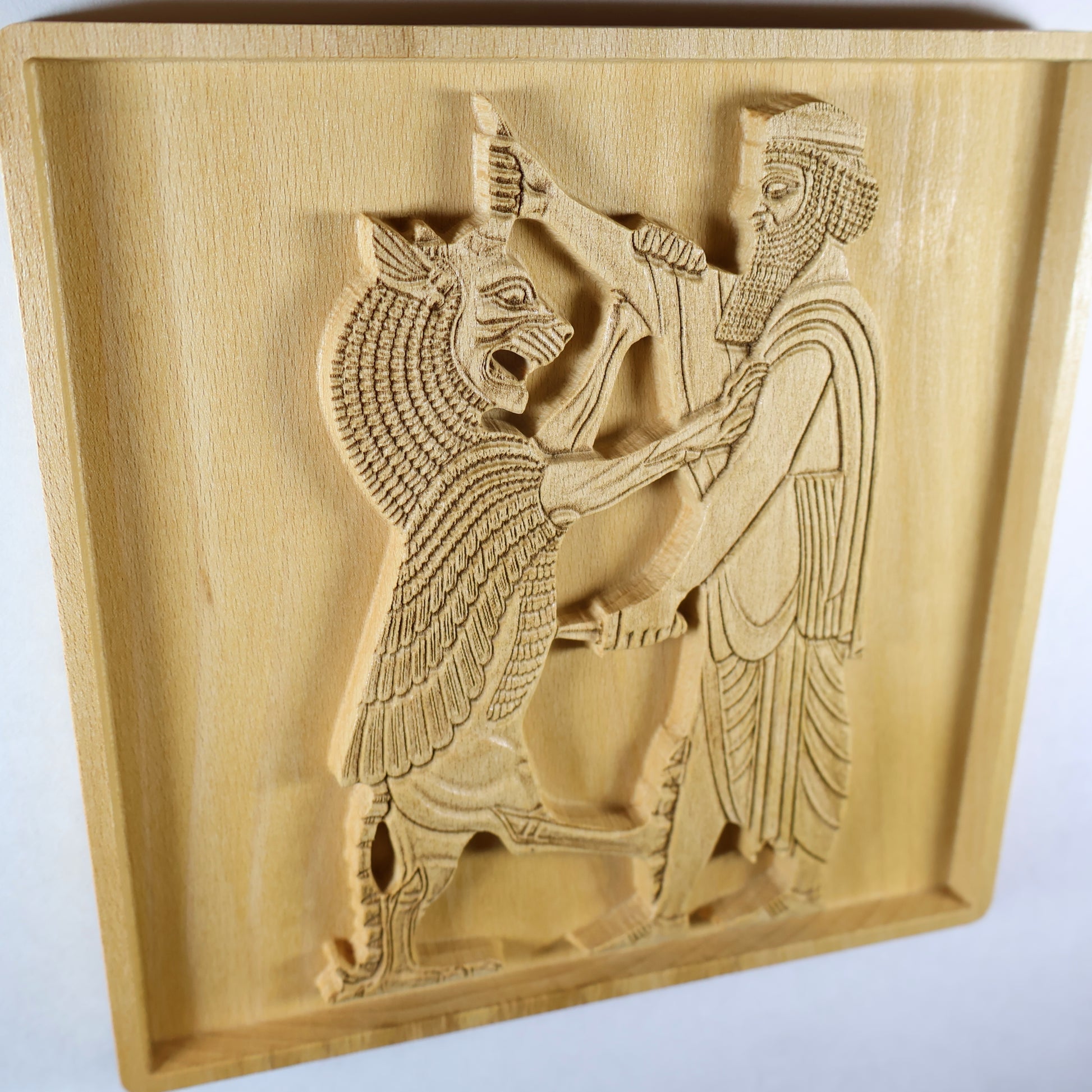 Side perspective of Shahriar and the Lion wood relief showing the raised Persian figure and lion carving, recessed square frame, carved robe lines, weapon detail, and natural beech wood finish.