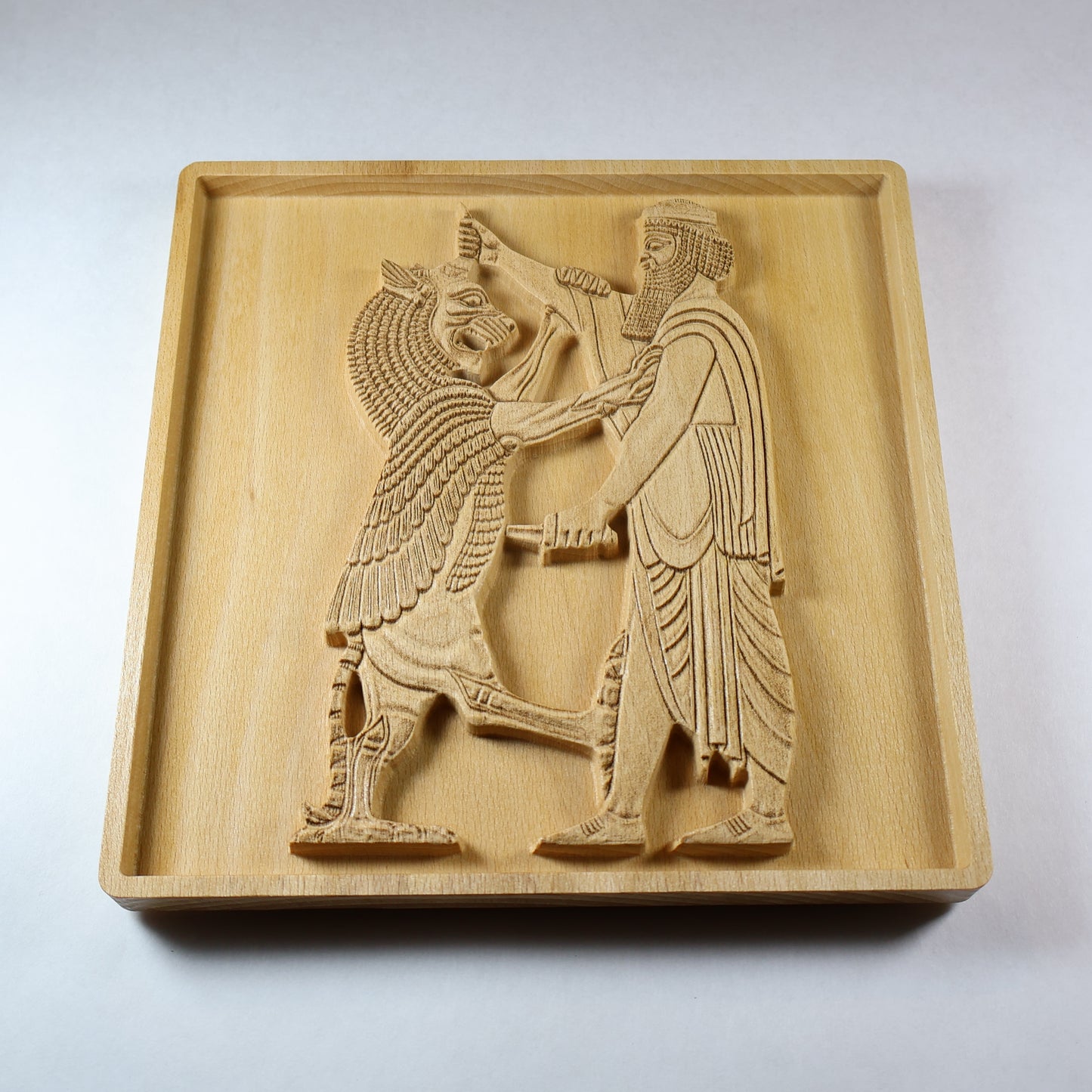 Three-quarter view of the Shahriar and the Lion wood relief showing the Persian figure, raised lion, carved weapon, robe folds, recessed frame, and natural beech wood finish.