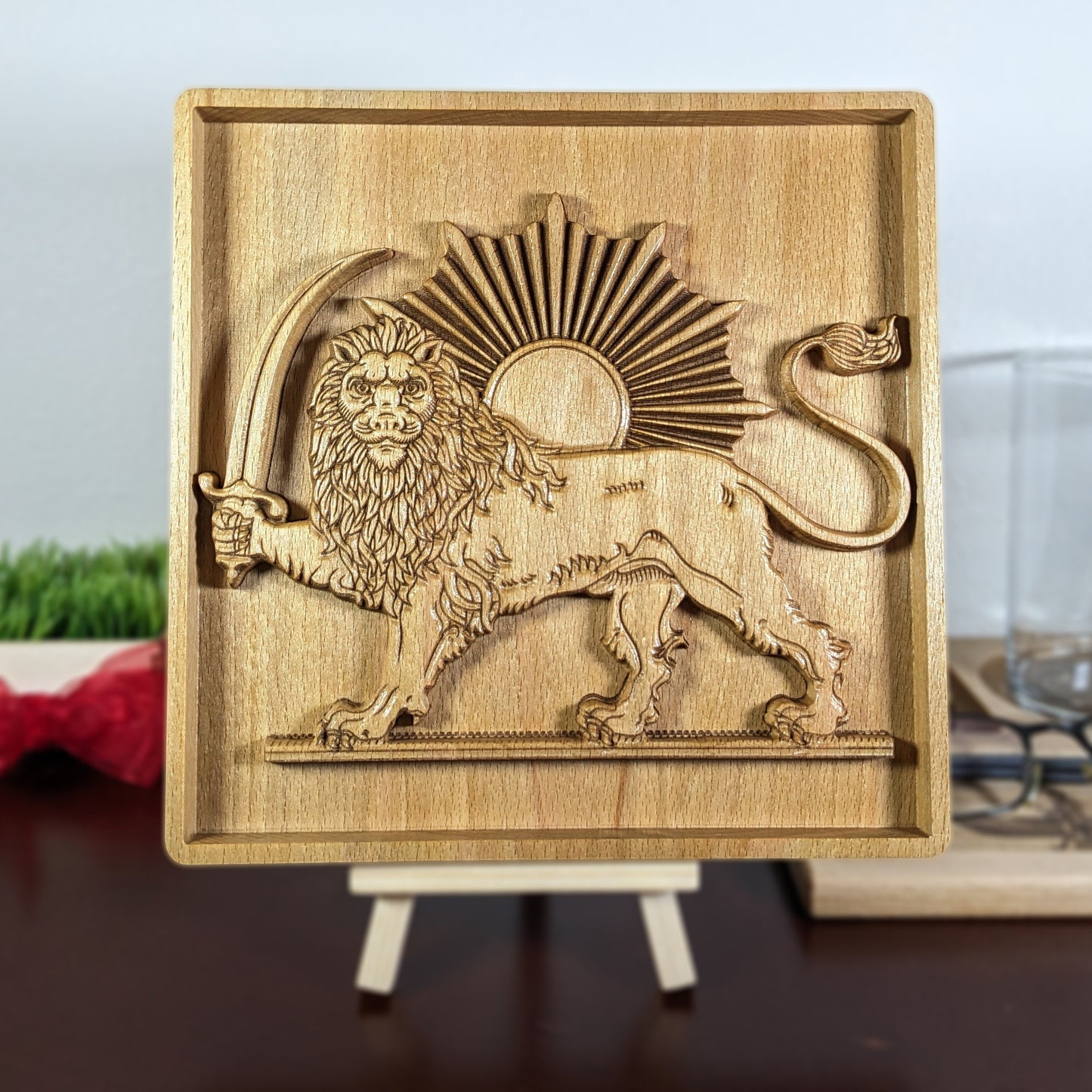Lion and Sun wood wall art displayed on a small easel, featuring a Persian carved wood relief with standing lion, raised sword, curved tail, sunburst rays, framed beech panel, and tabletop display for office, shelf, or home.