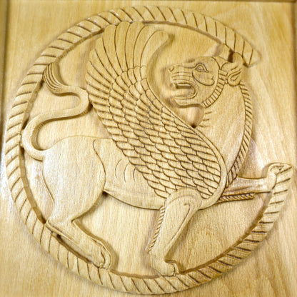 Straight front detail of a Persian griffin wood relief showing the circular winged lion design, carved feathers, lion paws, and natural wood finish.