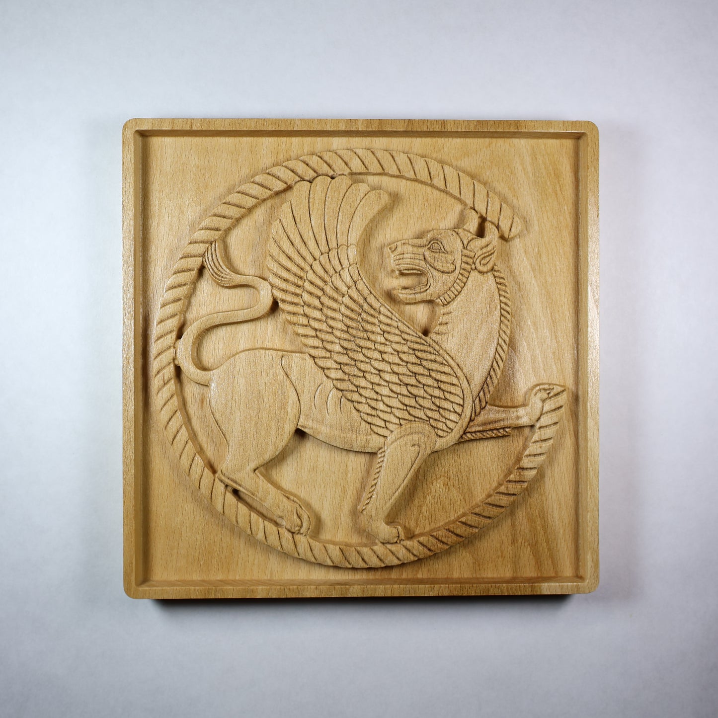 Front view of an Achaemenid Winged Lion Roundel wood relief with a carved Persian griffin, circular border, feathered wings, and natural wood finish.