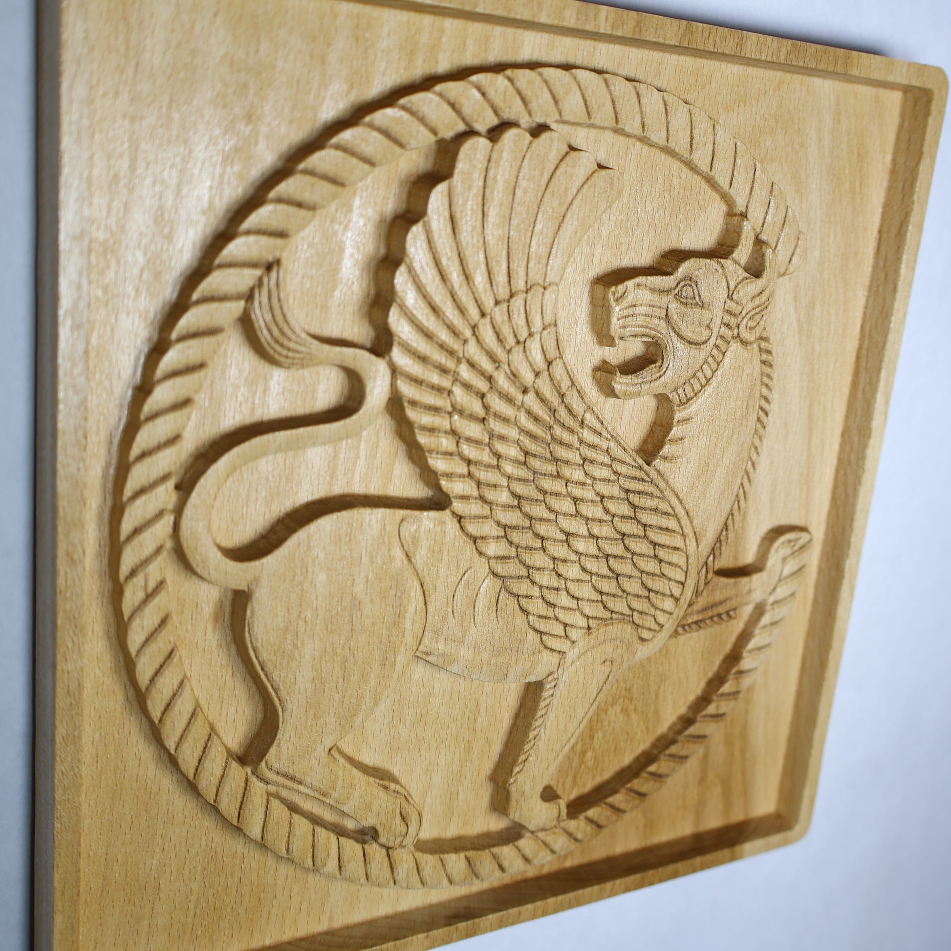 Display-angle view of a mythical lion wood relief showing the Persian griffin roundel, raised wing, carved mane, sweeping tail, and natural wood finish.