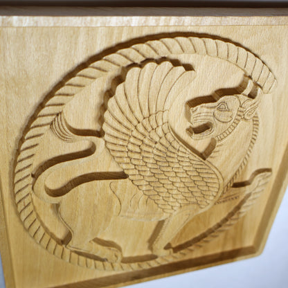 Close detail of a Persian guardian lion roundel showing the carved wing, animal face, circular border, fine linework, and natural wood grain.