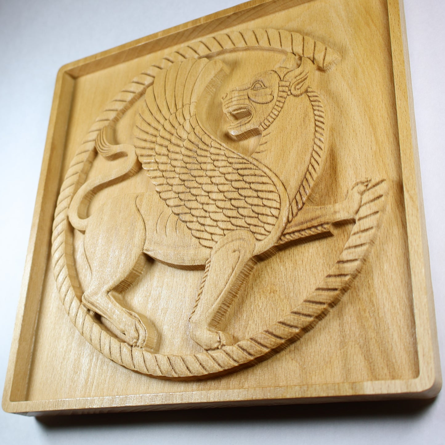 Angled view of an Achaemenid winged lion wood relief showing the carved guardian, roundel frame, feather details, and natural wood finish.