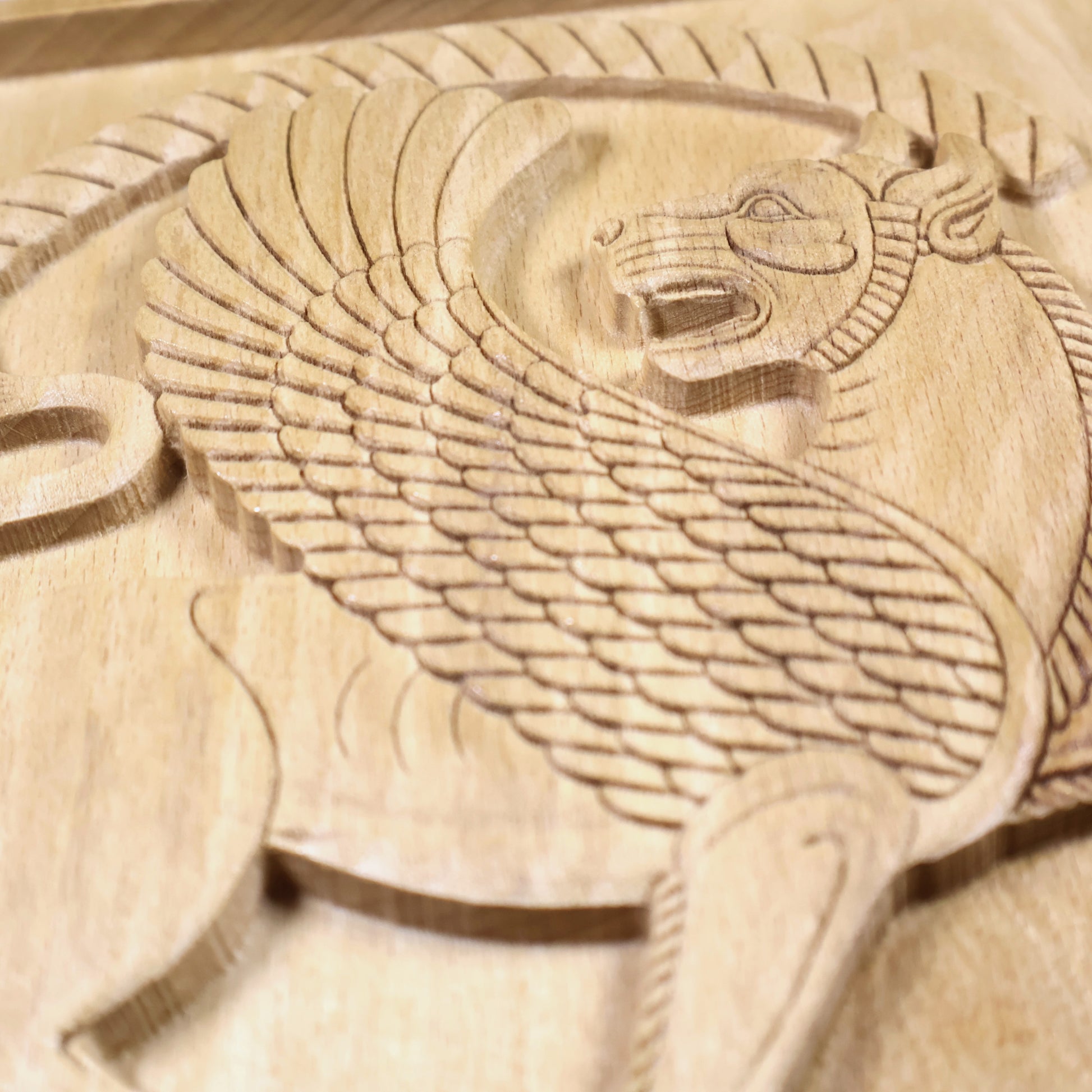 Close-up of a Shirdal inspired winged lion wood relief showing layered feathers, lion body, curved tail, round border, and natural wood grain.