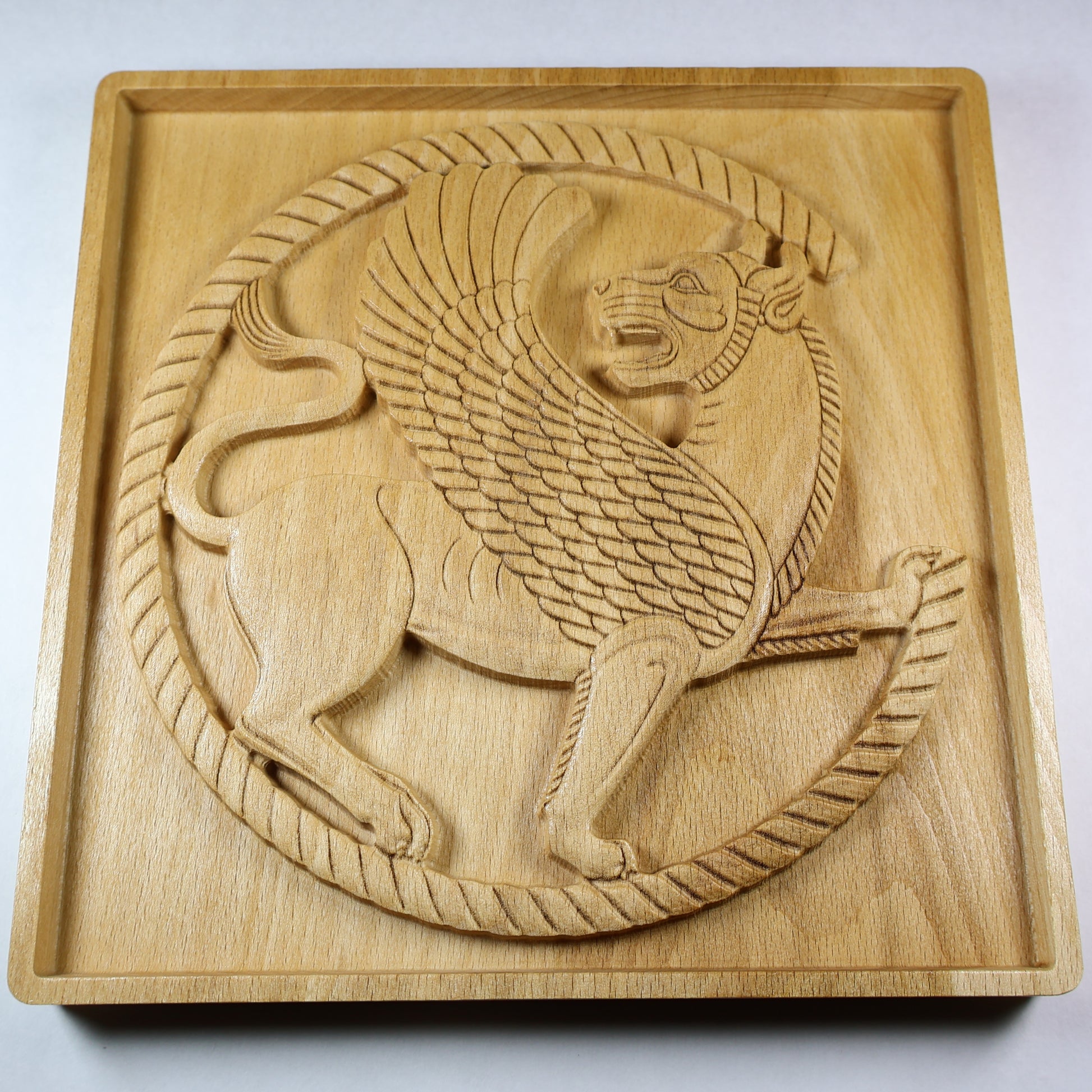 Low angled view of a Persian griffin wood relief showing the winged lion roundel, raised carving depth, feather details, and natural wood grain.