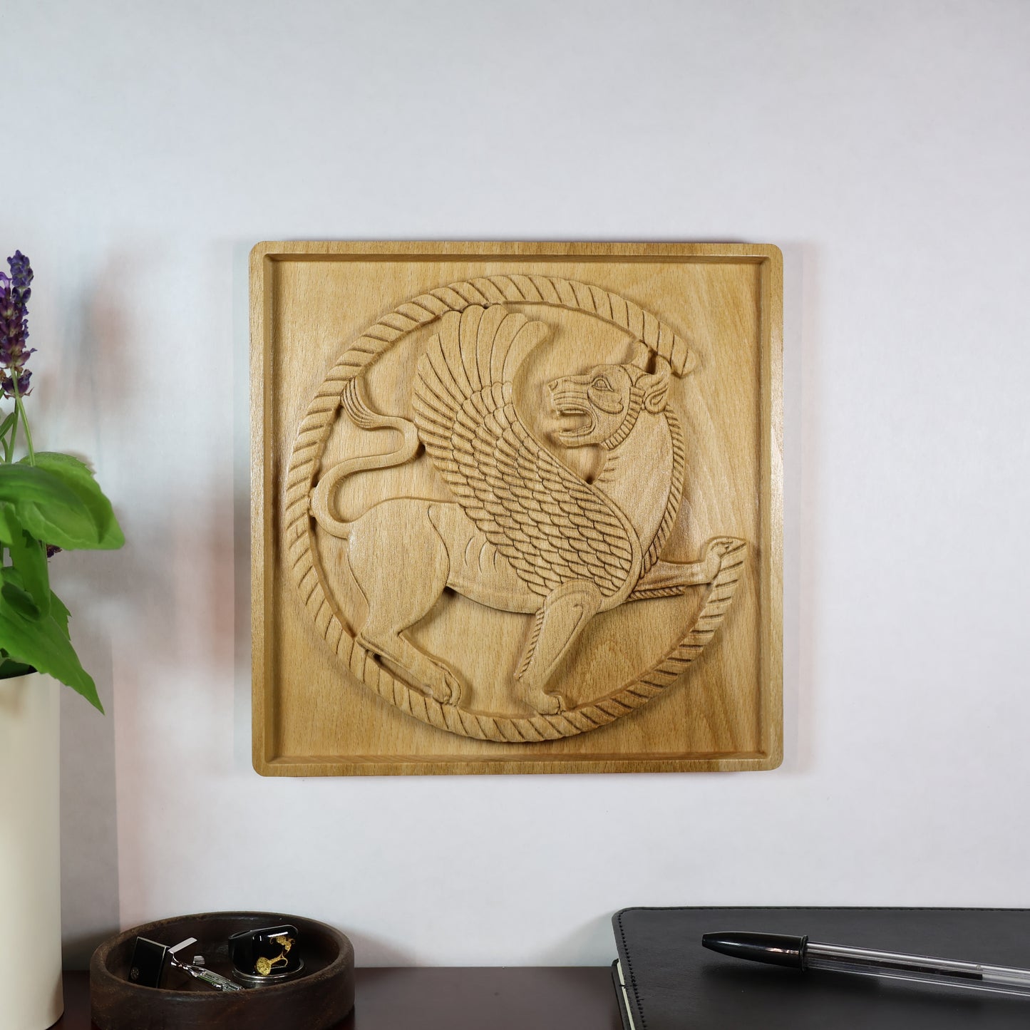 Achaemenid Winged Lion Roundel displayed on a wall in a room setting, showing the carved Persian guardian design and natural wood tone.