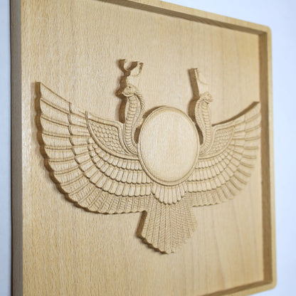 Side-angle view of an Egyptian Winged Sun Disk wood relief showing the raised sun disk, carved wings, twin cobras, feather details, and natural beech wood finish.
