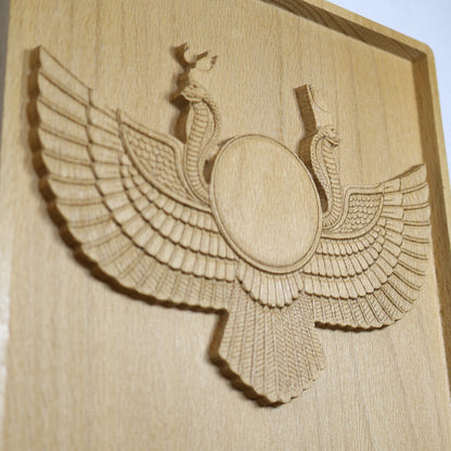 Close angled detail of an Egyptian Winged Sun Disk wood relief showing the central sun disk, twin cobras, feathered wings, lower tail, carved depth, and natural beech wood finish.