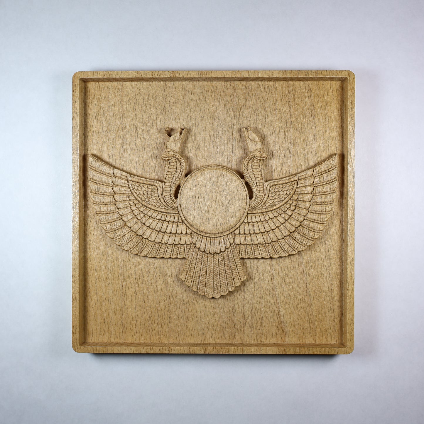 Front view of an Egyptian Winged Sun Disk wood relief with carved wings, mirrored cobra details, a central sun disk, square frame, and natural beech wood finish.